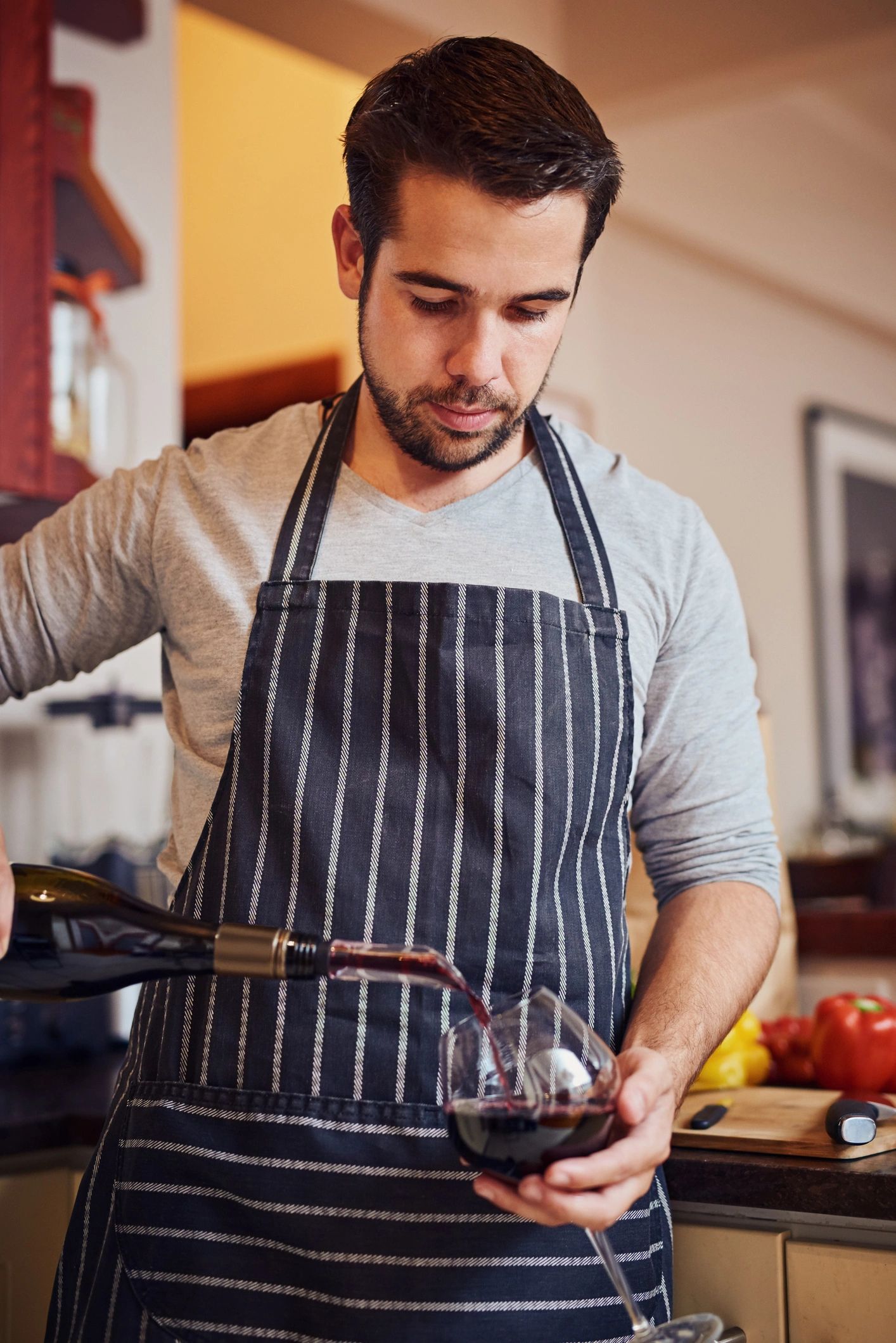 Happy young man pouring a glass of wine while cooking